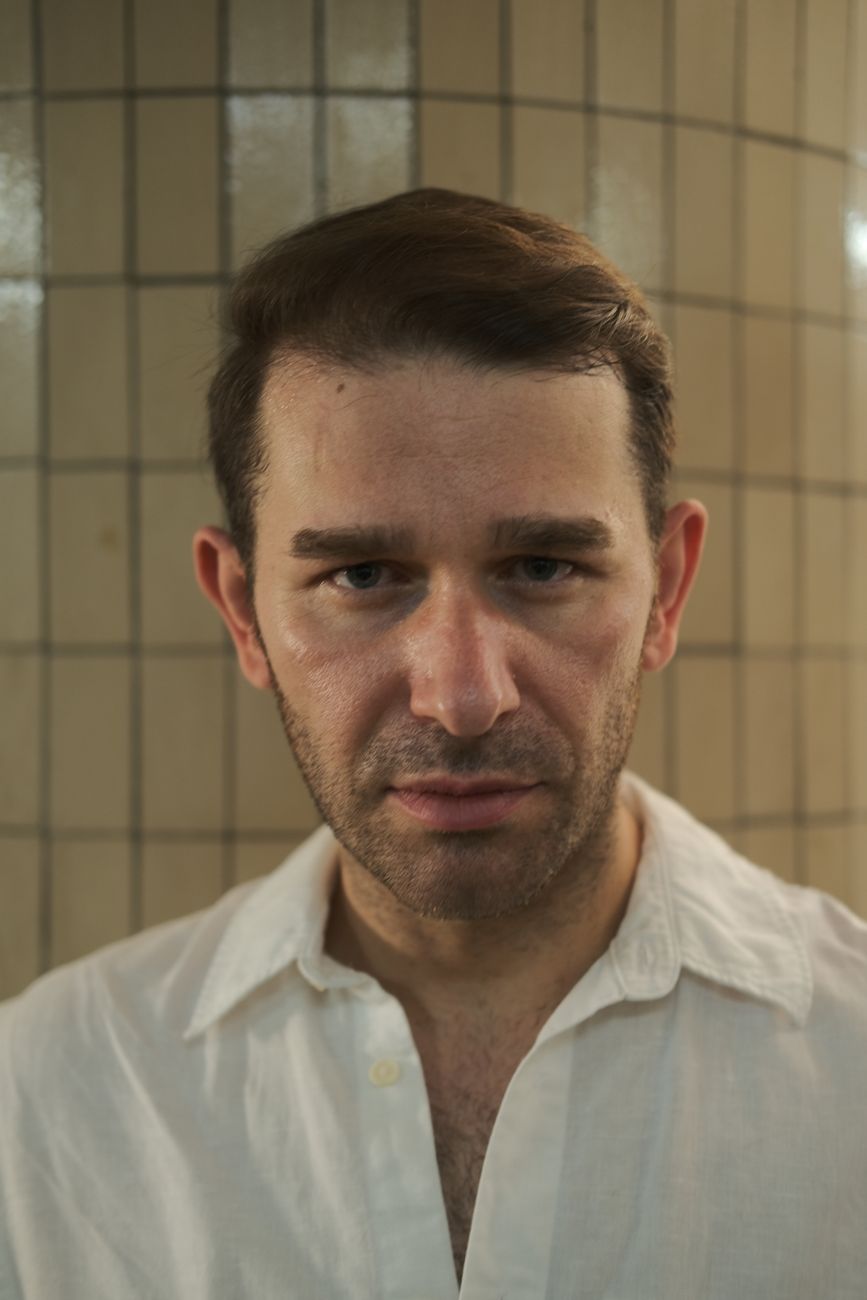 Homme aux tempes dégarnies, cheveux courts coiffés vers l'arrière, chemise blanche
