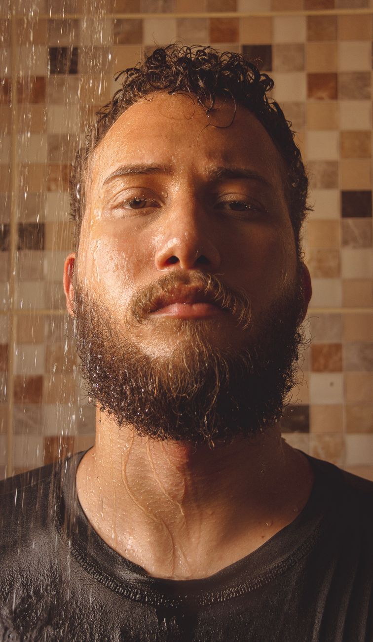 Homme à la barbe fournie et entretenue, de face devant un mur carrelé