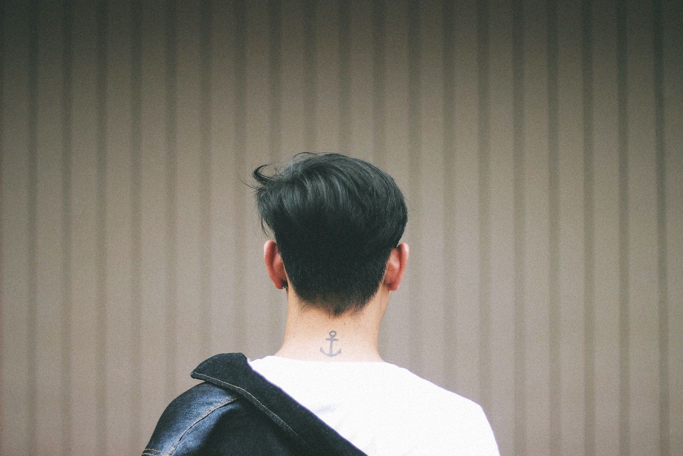 Homme vu de dos, nuque effilée en pointe au-dessus d'un petit tatouage d'ancre