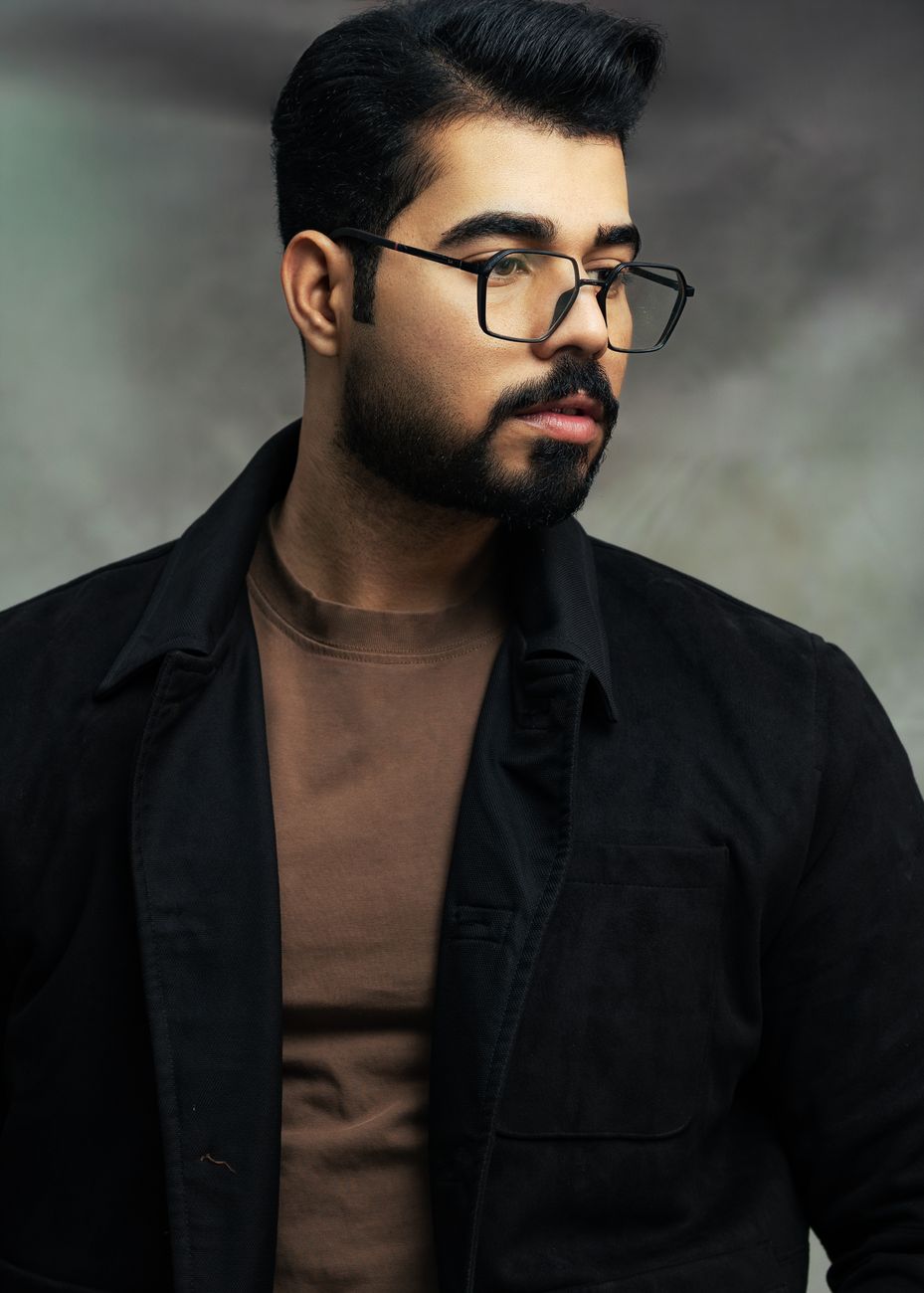 Homme barbu à lunettes, barbe courte et fournie, veste noire
