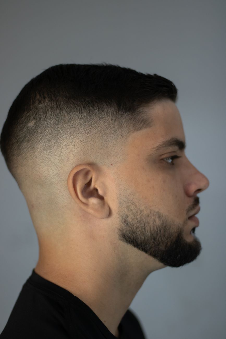 Homme barbu de profil, dessus court et côtés en dégradé net, sur fond gris
