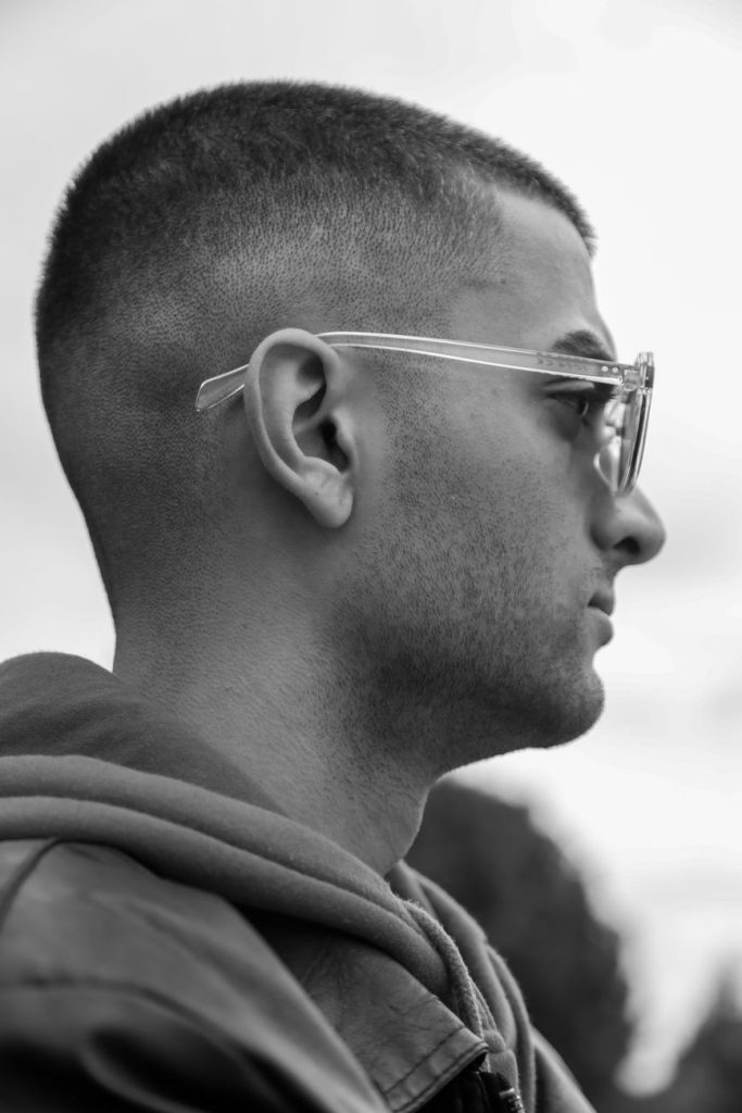 Homme à lunettes de profil, cheveux courts coupés presque à une seule hauteur, en noir et blanc
