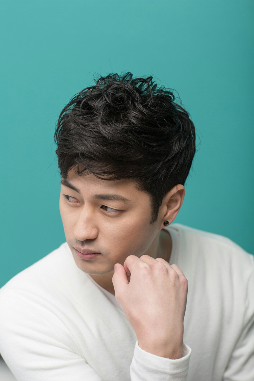 Homme asiatique aux cheveux noirs texturés, frange souple et côtés courts, de trois quarts sur fond bleu-vert