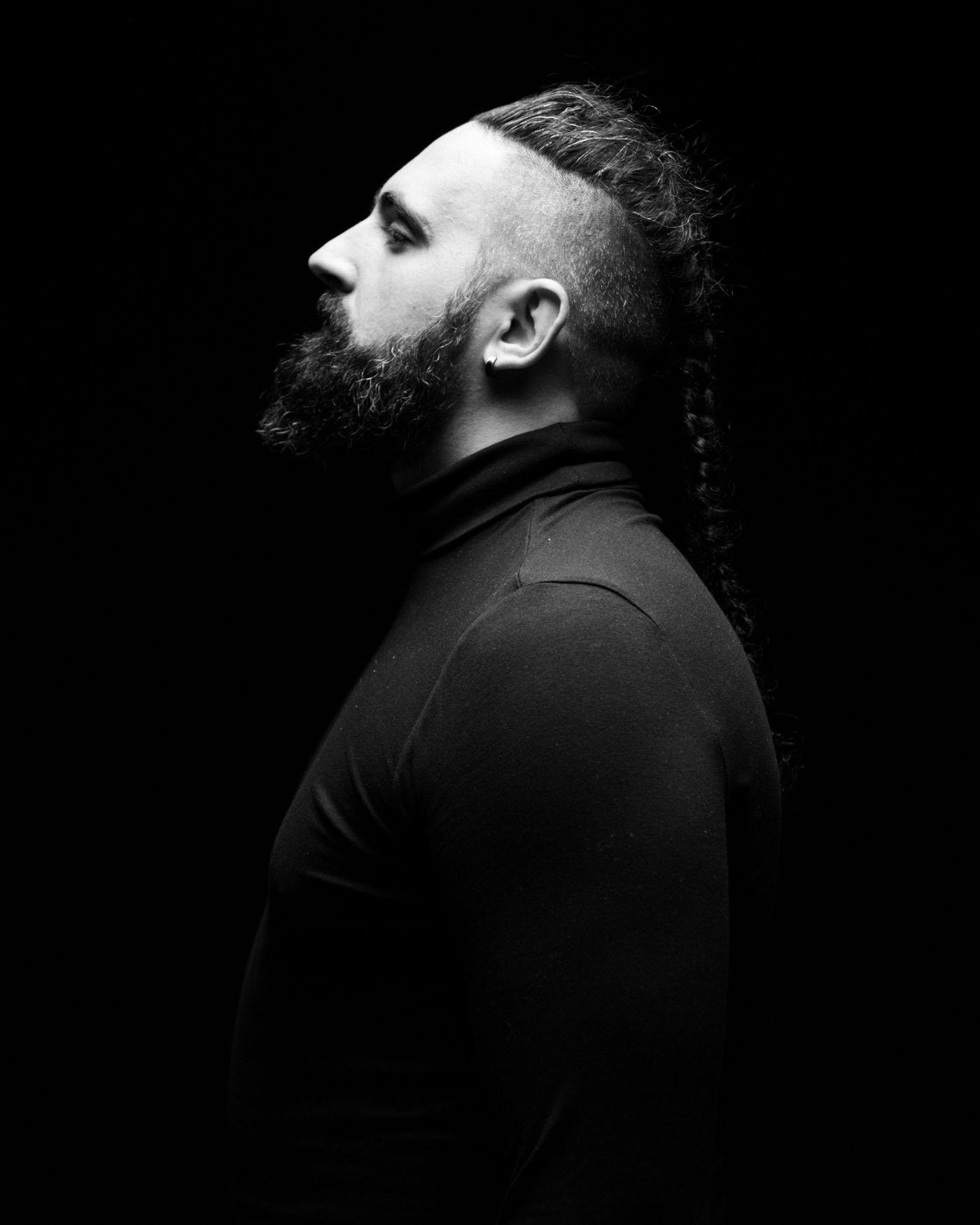 Profil en noir et blanc d'un homme barbu, côtés rasés et longue tresse sur le dessus