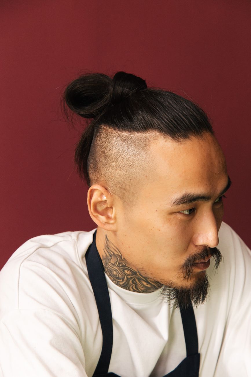 Homme asiatique au chignon haut, côtés rasés et barbe, tablier noir