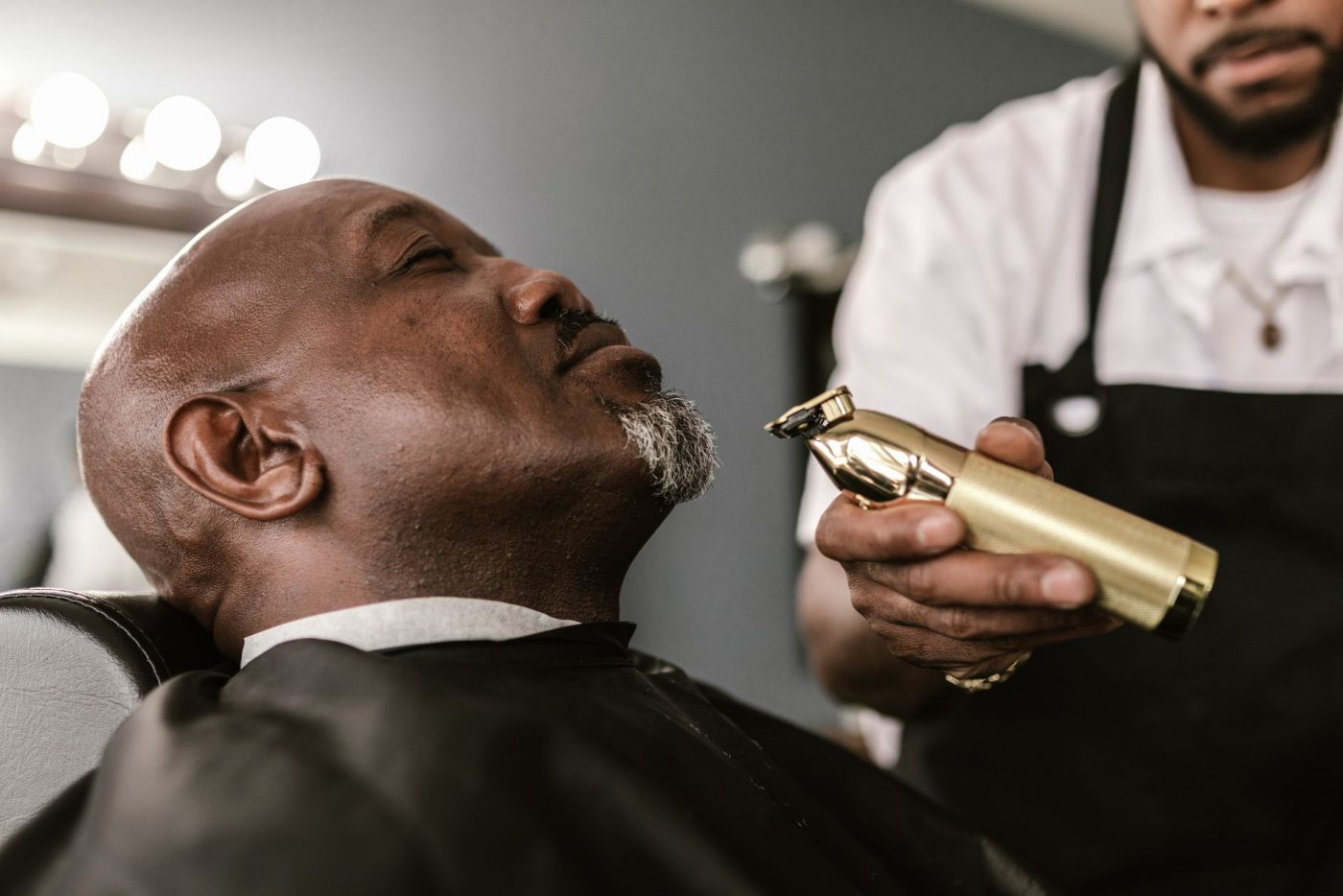 Barbier qui reprend les bords d’une barbe courte grise à la tondeuse de finition